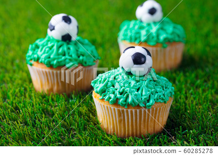 Football party, birthday decorated cupcake on green grass background. Close up. 60285278