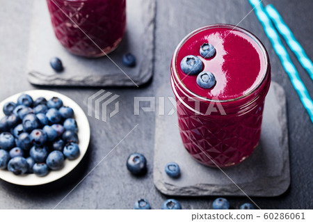 Berry acai smoothie with fresh blueberries on a black stone background. Berry acai smoothie with fresh blueberries on a black stone background. 60286061