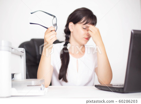 Girl business worker in the office holds glasses in hand. Concept of pain in the eyes from the computer, dry eye syndrome, accommodation spasm, office diseases Girl business worker in the office holds glasses in hand. Concept of pain in the eyes from the computer, dry eye syndrome, accommodation spasm, office diseases 60286203
