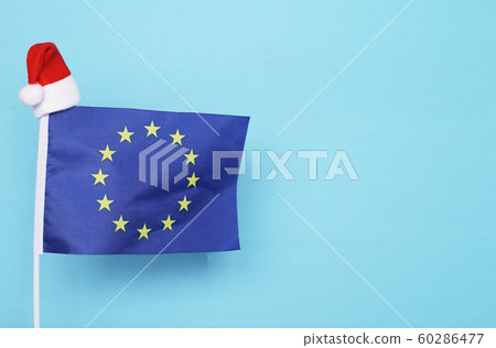 Flag of European Union with little santa claus hat on blue background. New Year winter holiday concept, copy space Flag of European Union with little santa claus hat on blue background. New Year winter holiday concept, copy space 60286477