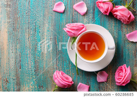 Cup of tea with pink rose. Colorful turquoise wooden background. Top view. Copy space. Cup of tea with pink rose. Colorful turquoise wooden background. Top view. Copy space. 60286685