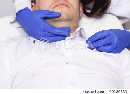 The doctor performs a double chin lift on a young man using the modern mesothread method, procedure 60286783