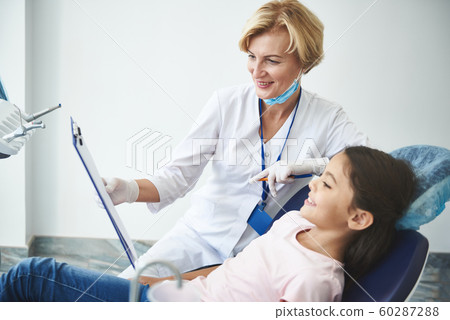 Optimistic dentist is showing diagnosis on clipboard to young patient Optimistic dentist is showing diagnosis on clipboard to young patient 60287288