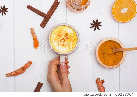 Woman's hand holding a cup with turmeric latt or golden milk on white table 60288364