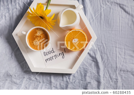 Tray with coffee, milk, orange and yellow flower on it standing on the bed 60288435