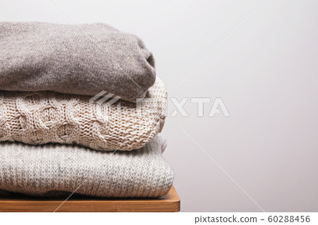 Stack of warm knitted woolen sweaters against white wall Stack of warm knitted woolen sweaters against white wall 60288456