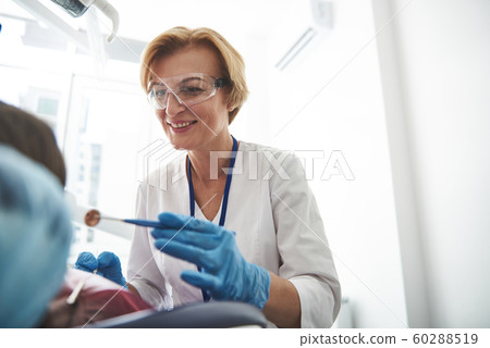 Cheerful nice female dentist treating teeth with pleasure 60288519