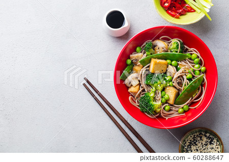 Soba noodles with vegetables and fried tofu in a bowl. Grey background. Top view. Copy space. Soba noodles with vegetables and fried tofu in a bowl. Grey background. Top view. Copy space. 60288647