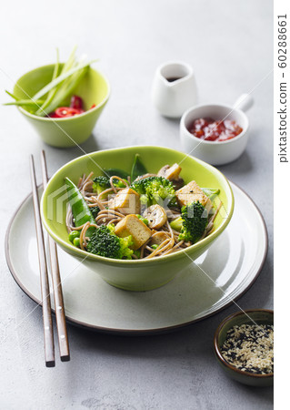 Soba noodles with vegetables and fried tofu in a bowl. Grey background. Soba noodles with vegetables and fried tofu in a bowl. Grey background. 60288661