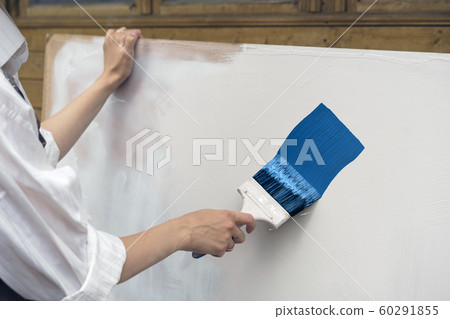 Female hand painting a white sheet of plywood by blue paint Female hand painting a white sheet of plywood by blue paint 60291855