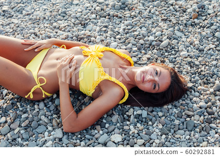 Beautiful woman with long hair in a yellow swimsuit walks on the beach by the sea Beautiful woman with long hair in a yellow swimsuit walks on the beach by the sea 60292881