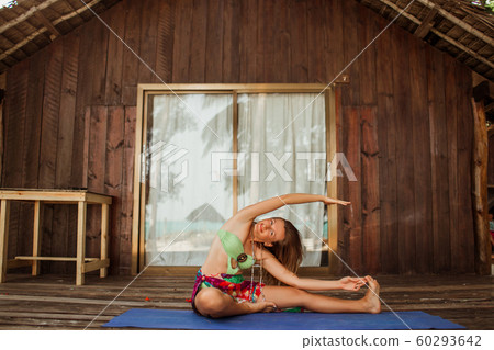 Yoga asana by young beautiful woman is sitting near wooden house in the tropical paradise with palms and banana trees on Zanzibar island Yoga asana by young beautiful woman is sitting near wooden house in the tropical paradise with palms and banana trees on Zanzibar island 60293642