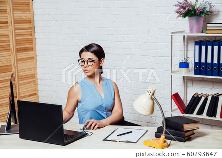 business girl sits in an Office behind a desk with a computer 60293647