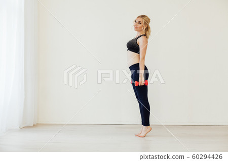 Blonde woman engaged in fitness with dumbbells in sports hall 60294426