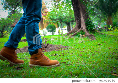 Body part a man wearing jean and walking.He is walking on grass in public park.going,walking,objective,goal. 60294919