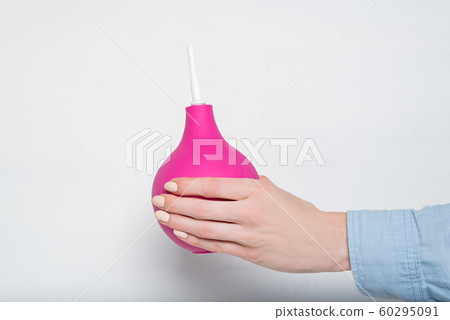 Big pink enema in a female hand. White background. Big pink enema in a female hand. White background. 60295091