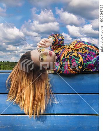 Girl with her hair lies on a fence against the sky Girl with her hair lies on a fence against the sky 60304735