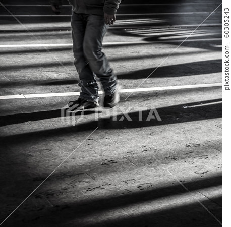 Black young man walking alone in urban city with light and dark shadows - Concept of loneliness 60305243