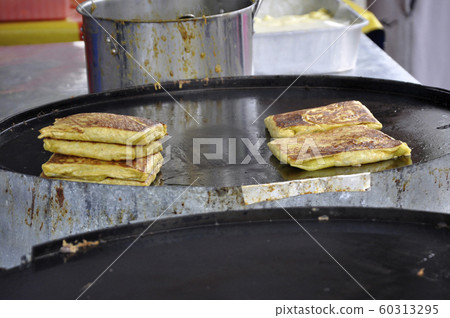 Malaysian street food called Murtabak. Cook by Hawkers. In it there is a mixture of meat, eggs and onions. Eaten with a special gravy. Malaysian street food called Murtabak. Cook by Hawkers. In it there is a mixture of meat, eggs and onions. Eaten with a special gravy. 60313295