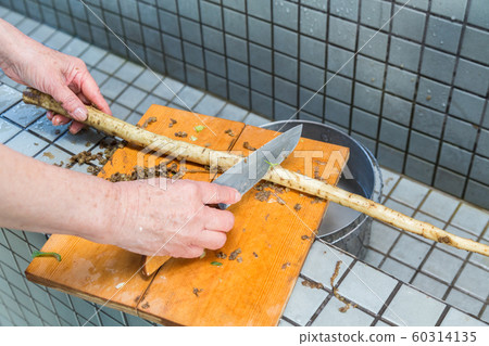 Senior woman skinning burdock at campsite 60314135