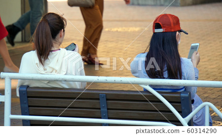 Two women who handle smartphones on a bench Two women who handle smartphones on a bench 60314290