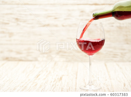 Pour red wine into a glass on white wooden 60317383
