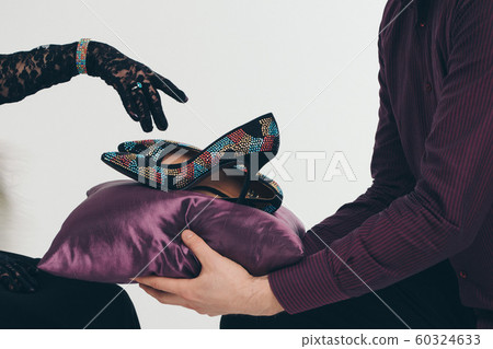The shoes in jewels on a purple pillow. A man brings shoes to a girl, she points her finger at them in a black glove. The shoes in jewels on a purple pillow. A man brings shoes to a girl, she points her finger at them in a black glove. 60324633