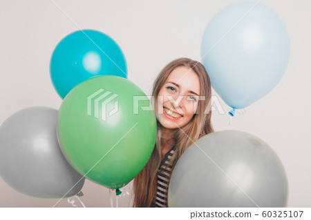 blonde girl smiling and looking at camera between multicolored balls on white background. Studio portrait of attractive girl waiting for birthday party. Face and balloons blonde girl smiling and looking at camera between multicolored balls on white background. Studio portrait of attractive girl waiting for birthday party. Face and balloons 60325107
