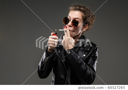 Caucasian girl with rough facial features in a black jacket lights a cigarette isolated on black Caucasian girl with rough facial features in a black jacket lights a cigarette isolated on black 60327265