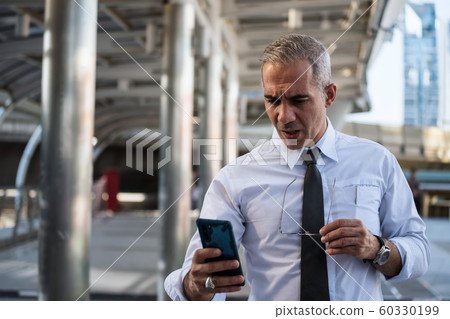 Anxious old businessman read news by smartphone Anxious old businessman read news by smartphone 60330199