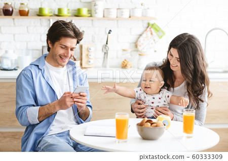 Millennial man texting on phone, dining with wife and baby Millennial man texting on phone, dining with wife and baby 60333309
