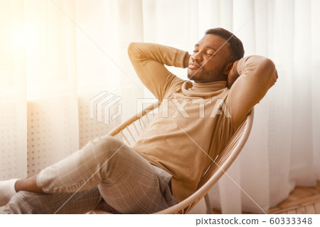 Peaceful Black Man Sitting On Modern Chair At Home Peaceful Black Man Sitting On Modern Chair At Home 60333348