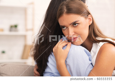 Girl Rolling Eyes Embracing Crying Friend Sitting On Sofa 60333355