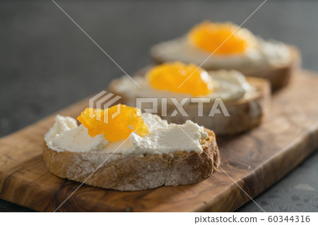 Three ciabatta slices with ricotta and orange marmalade on olive wood board on terrazzo surface Three ciabatta slices with ricotta and orange marmalade on olive wood board on terrazzo surface 60344316