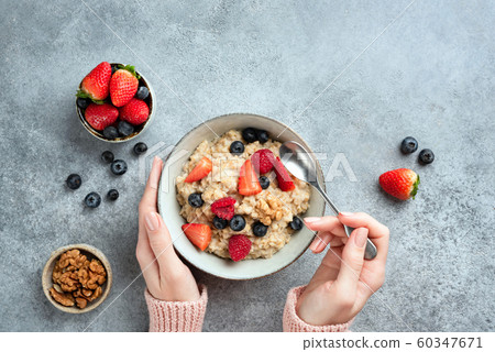 Oatmeal porridge bowl with berries in female hands Oatmeal porridge bowl with berries in female hands 60347671