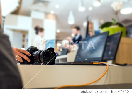 Hand of the camera operator touching a modern DSLR camera placed on the office desk. 60347740