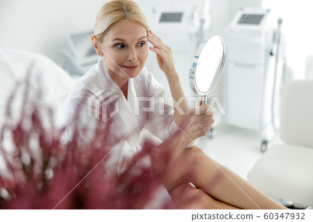 Smiling woman looking at the condition of the skin of the face 60347932