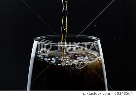 Glass of pouring fizzy drink with ice on a black background 60348564