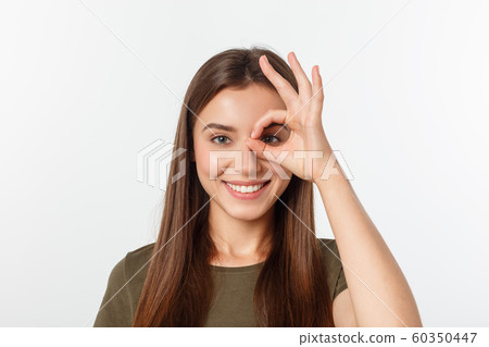 Young woman with ok sign on eye isolate over grey background. Young woman with ok sign on eye isolate over grey background. 60350447
