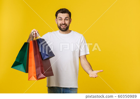 Photo of happy guy, holding shopping bags, isolated over yellow background 60350989