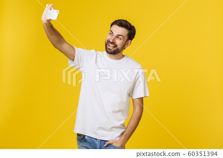 Closeup of young handsome man looking at smartphone and taking selfie. isolate over yellow background. 60351394