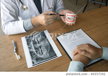Asian dentist holding pen pointing to the dentures Asian dentist holding pen pointing to the dentures 60357342