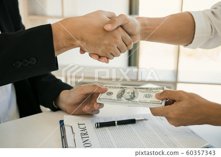 Two corporate businessmen shaking hands while one Two corporate businessmen shaking hands while one 60357343