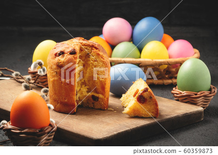 Easter cake on a cutting board and colored eggs on a table and in a wicker basket - traditional Easter breakfast Easter cake on a cutting board and colored eggs on a table and in a wicker basket - traditional Easter breakfast 60359873