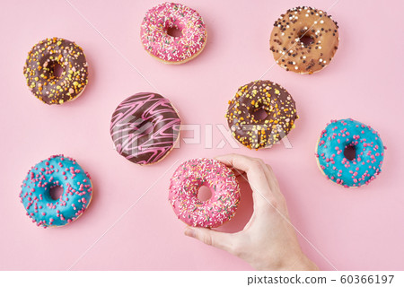 Woman hand take color donut on a pink background. Woman hand take color donut on a pink background. 60366197