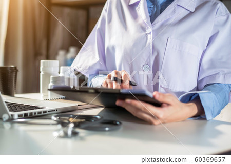 Doctor working on laptop computer, writing prescription clipboard with record information paper folders on desk in clinic, Healthcare and medical concept. Focus on stethoscope. Doctor working on laptop computer, writing prescription clipboard with record information paper folders on desk in clinic, Healthcare and medical concept. Focus on stethoscope. 60369657