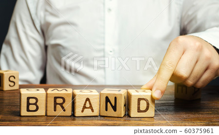 Businessman puts wooden blocks with the word Brand. Business, marketing, and advertising. Name, term, design, symbol that identifies one seller's good or service. Businessman puts wooden blocks with the word Brand. Business, marketing, and advertising. Name, term, design, symbol that identifies one seller's good or service. 60375961