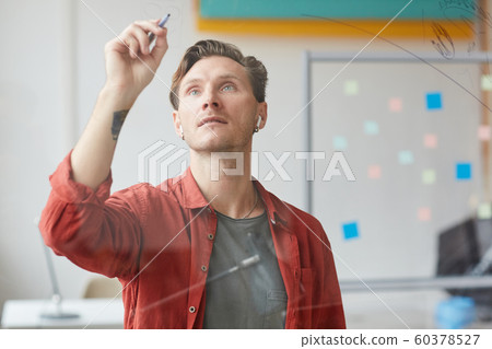 Tattooed Man Writing on Glass Wall in Office Tattooed Man Writing on Glass Wall in Office 60378527