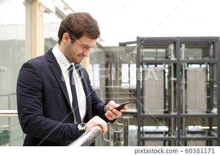 Happy businessman standing in office interior with smartphone in hands Happy businessman standing in office interior with smartphone in hands 60381171