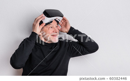 Portrait of a cheerful senior man with VR goggles in a studio. Portrait of a cheerful senior man with VR goggles in a studio. 60382446
